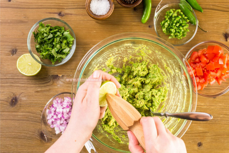 Mani spremono succo lime con spremiagrumi nella ciotola con polpa di avocado schiacciata