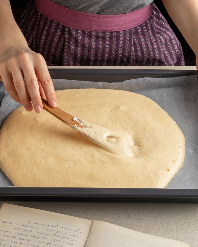 mani donna livellano impasto pan di spagna con spatola su teglia con carta forno
