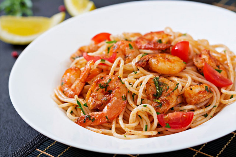 spaghetti con gamberi saltati i padella su piatto porcellana bianca spicchi limone prezzemolo