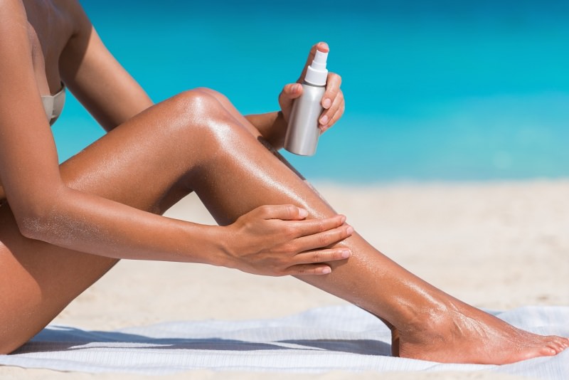 protezione solare spray su pelle abbronzata corpo donna costume da bagno due pezzi estate mare spiaggia