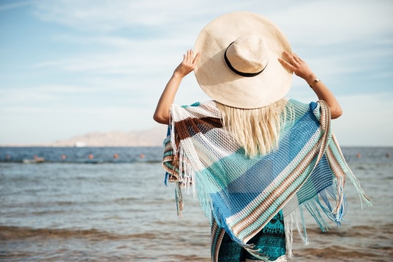 donna di spalle con cappello e poncho frange in riva al mare estate prova costume