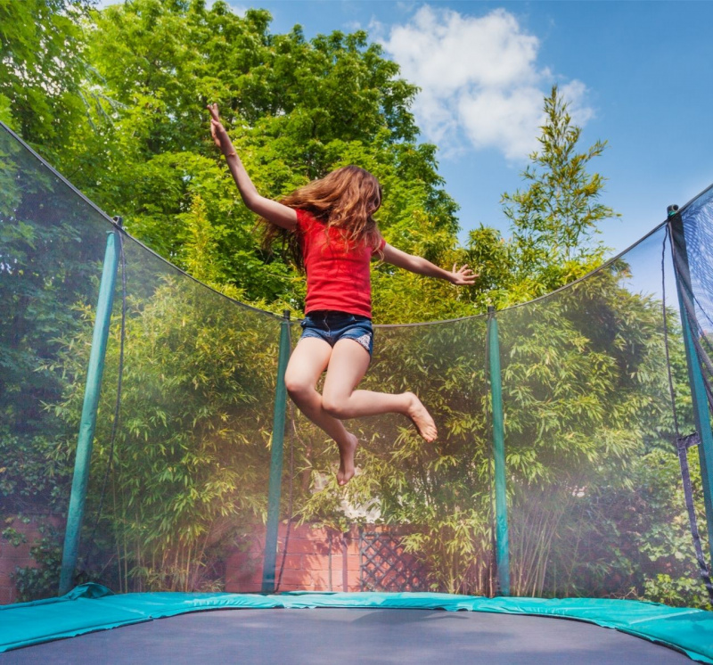 giovane ragazza salta sul trampolino tappeto elastico giardino alberi