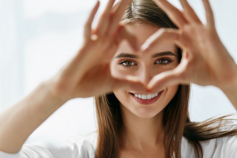 ragazza forma un cuore con le dita delle mani davanti agli occhi donna sorriso