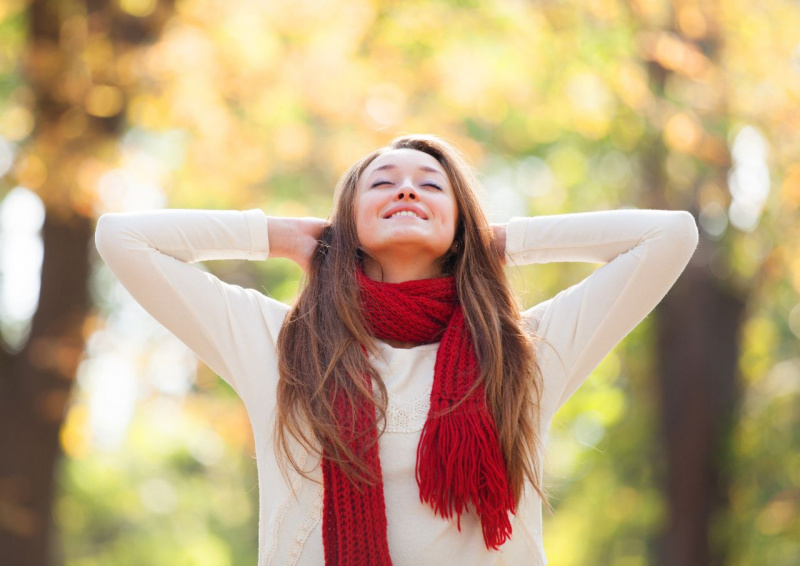 giovane donna indossa sciarpa rossa di lana su maglione bianco mani dietro la nuca all'aperto aria