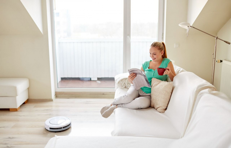 bella donna legge giornale sul sofà mentre robot aspira pavimento stanza pulita pulizie
