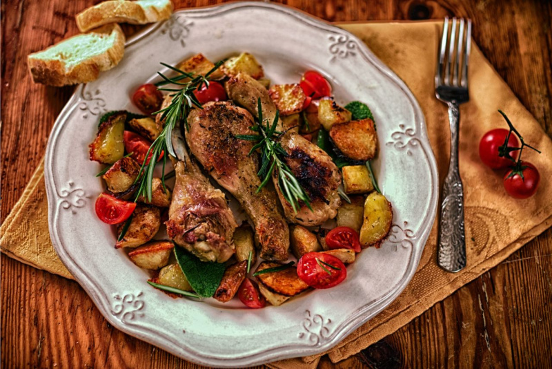piatto pronto cosce di pollo alla diavola con croccanti patate al forno e pomodori su tavolo legno forchetta tovagliolo
