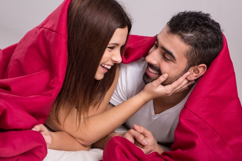 uomo donna letto sotto piumone rosso sorrisi