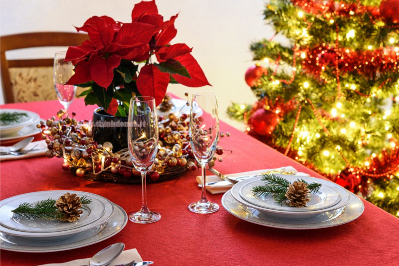 tavola apparecchiata festa di Natale calici flute tovaglia rossa piatti porcellana bianca segnaposto pigna rametti abete centrotavola natalizia