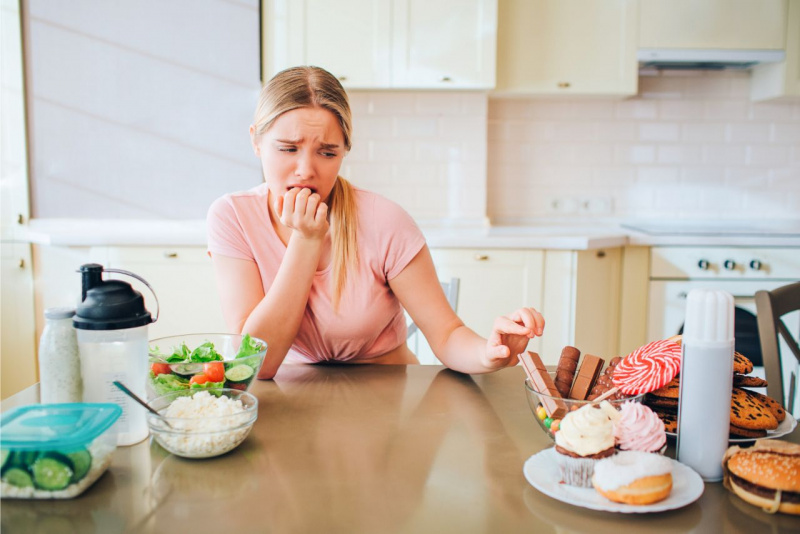 dieta stress tentazioni dolci giovane donna preoccupata maglietta rosa capelli lunghi lisci biondi cioccolato muffin 