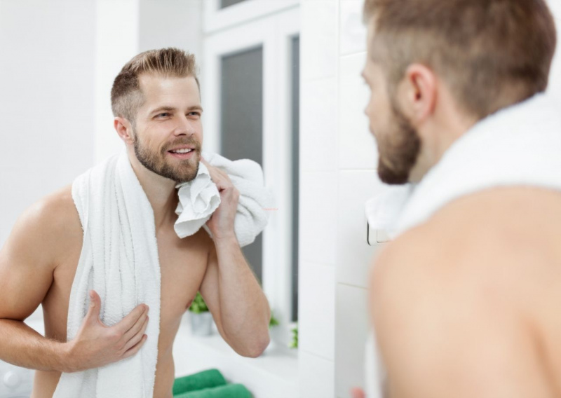 giovane uomo bello attraente barba sorriso allo specchio telo spugna routine mattino