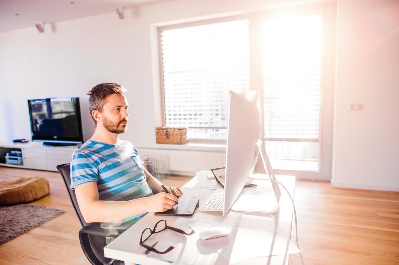 uomo alla scrivania lavoro da casa soggiorno smart working computer monitor luce finestra