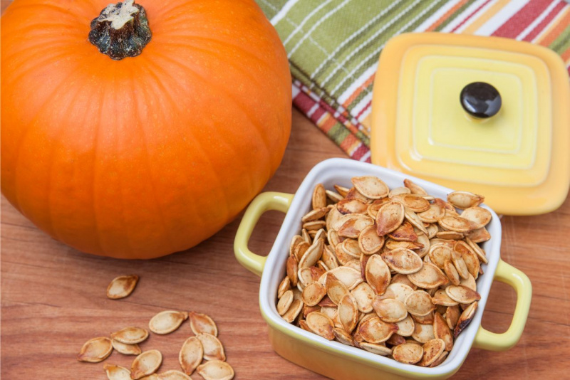 zucca arancione pentola ceramica piena di semi tostati arrostiti con coperchio asciugapiatti cotone